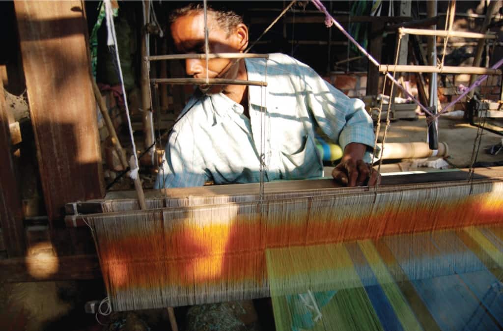 Chandabrati-man-at-loom-adjusting Working at a loom - Chhandabrati Weavers
